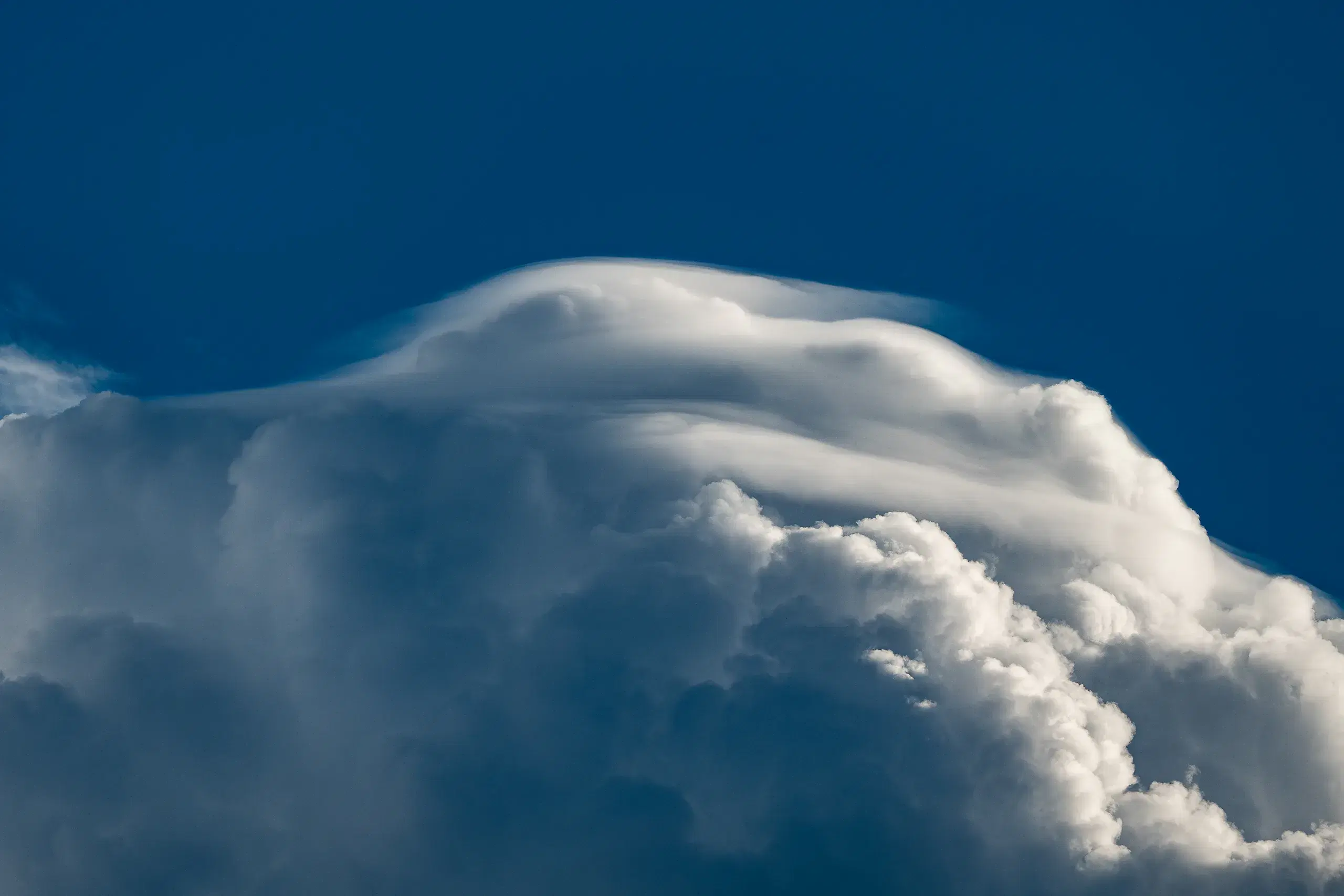 The anvil of a thunderhead catching late light above a deep blue sky.